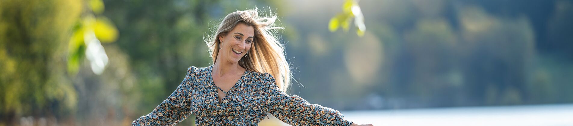 Frau spaziert lachend am Seeufer entlang