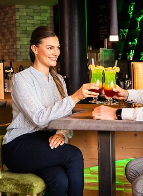 Pärchen an der Bar stoßen mit buntem Cocktail an