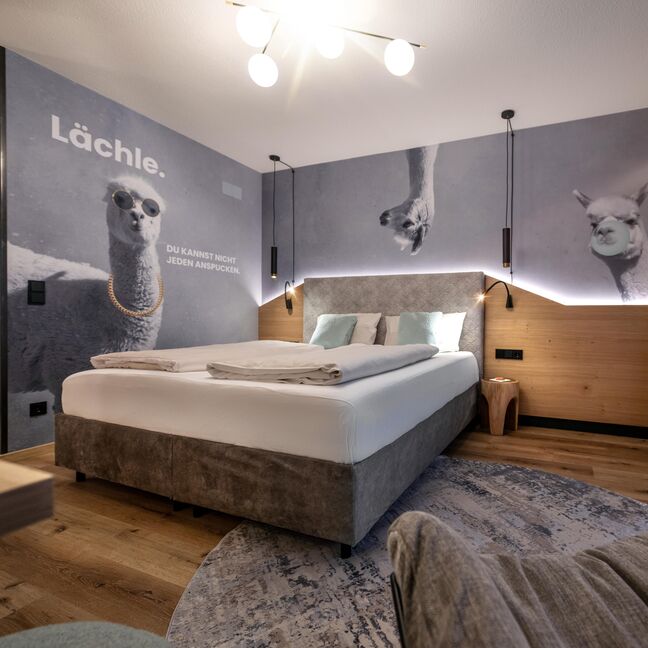 Boxspringbett mit lustiger Alpaka-Tapete im Hintergrund