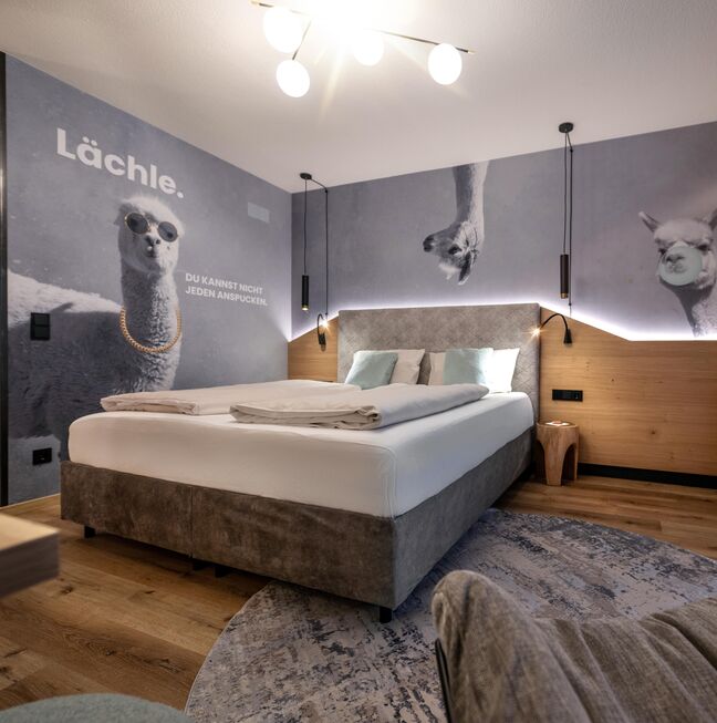 Boxspringbett mit lustiger Alpaka-Tapete im Hintergrund