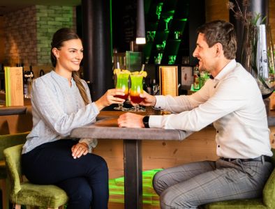 Pärchen an der Bar stoßen mit buntem Cocktail an