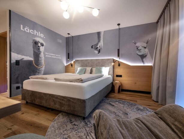 Boxspringbett mit lustiger Alpaka-Tapete im Hintergrund