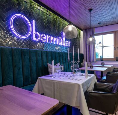 Grün geflieste Wand im Restaurant mit beleuchtetem Obermüller-Logo, davor ein festlich gedeckter Tisch