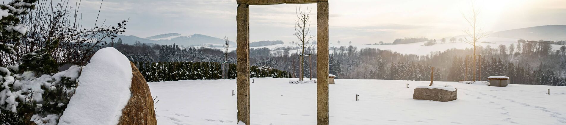 Winterlicher Wellnessgarten mit steinernem Torbogen und Sonnenuntergang