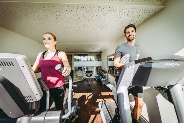 Pärchen trainiert auf Laufband und Crosstrainer im Fitnessraum