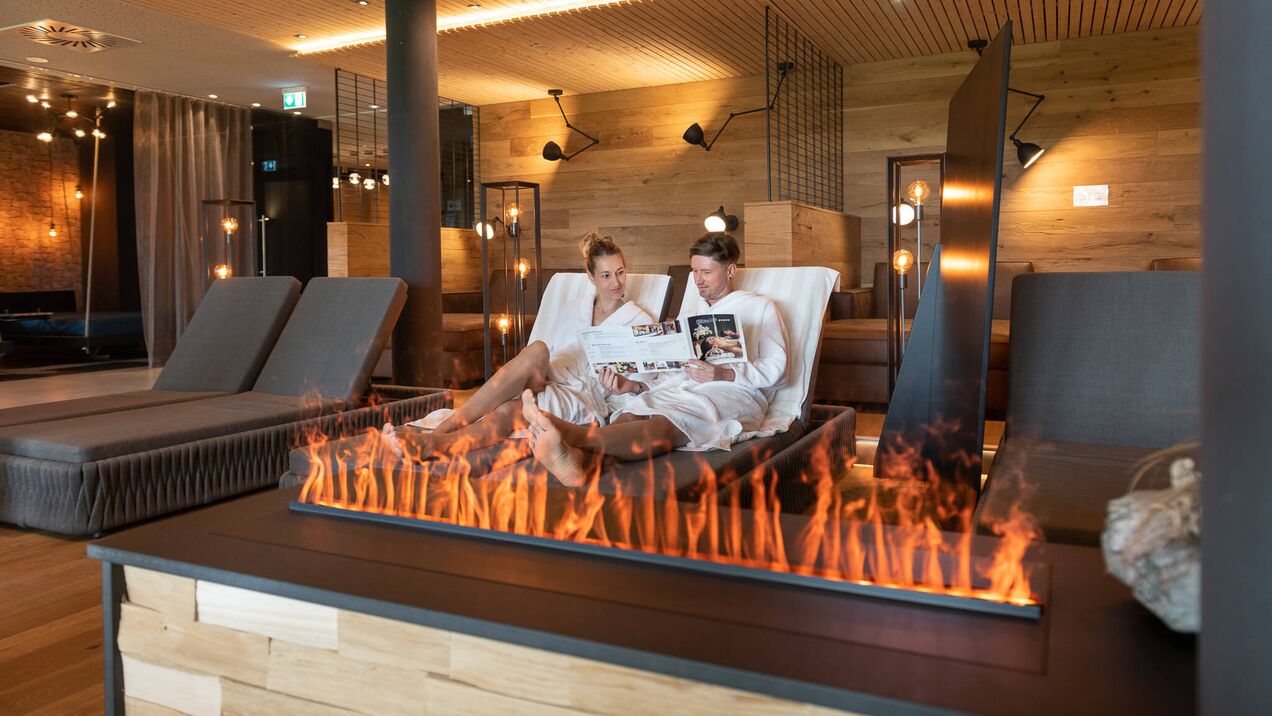 Paar relaxt auf einer Liege im Ruheraum vor Kamin