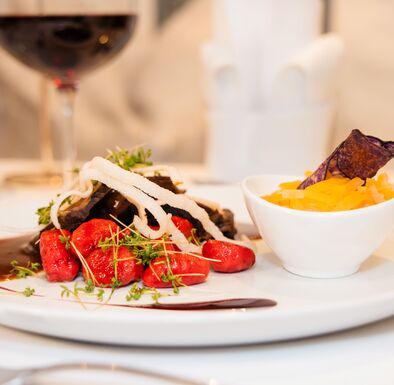Ein Teller mit Schmorbraten, roten Gnocchi und Tagliatelle und ein Glas Rotwein