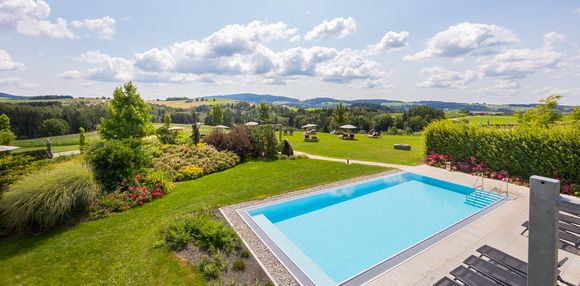 Blick auf Außenpool mit Landschaft & Garten zur Südseite des Balancehotels Obermüller Blick auf Außenpool mit Landschaft & Garten zur Südseite des Balancehotels Obermüller bei schönem Wetter mit einigen luftigen Wolken im Hintergrund