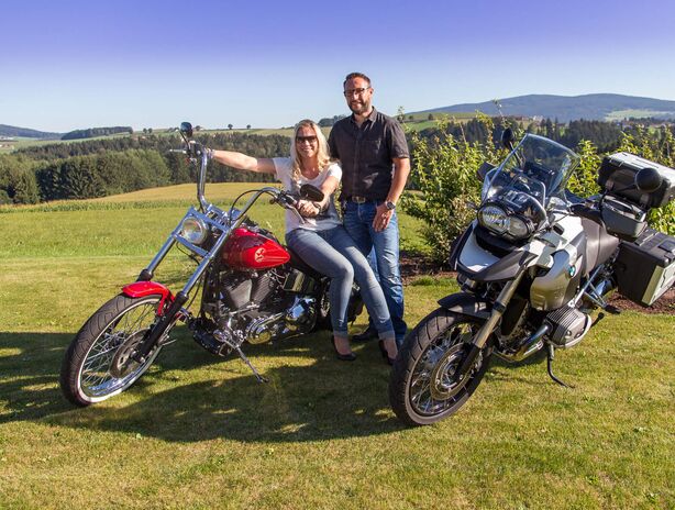 Paar sitzt auf Motorrad, welches im Wellnessgarten steht