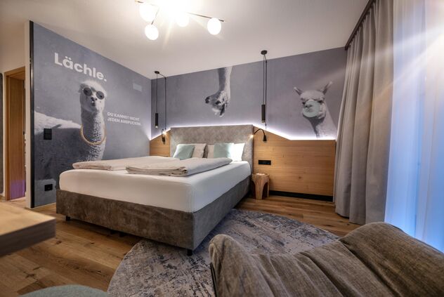 Boxspringbett mit lustiger Alpaka-Tapete im Hintergrund