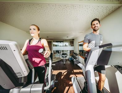 Pärchen trainiert auf Laufband und Crosstrainer im Fitnessraum
