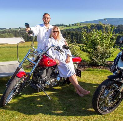 Pärchen im Bademantel auf Motorrad im Wellnessgarten