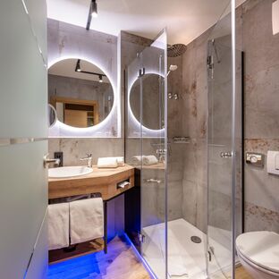 Modernes Badezimmer, grau gefliest mit rundem beleuchteten Spiegel