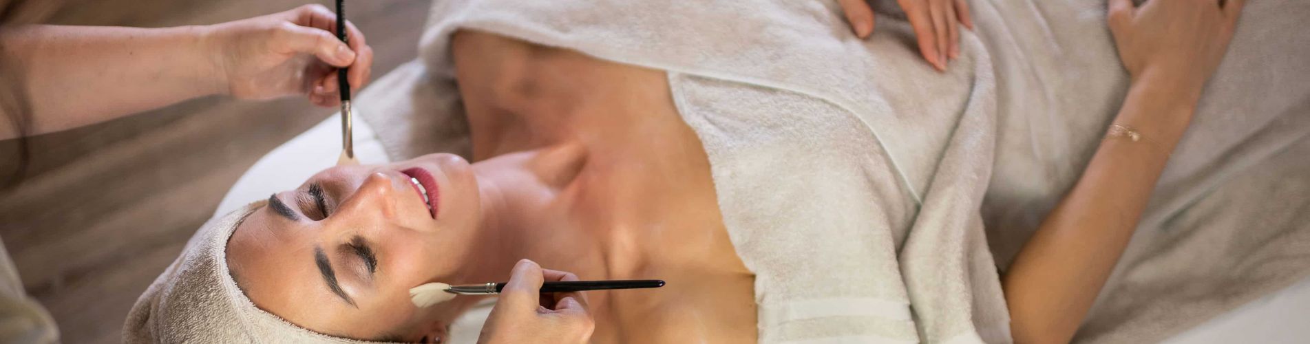Kosmetikerin trägt mit weichen Pinseln ein Produkt auf das Gesicht einer Dame auf