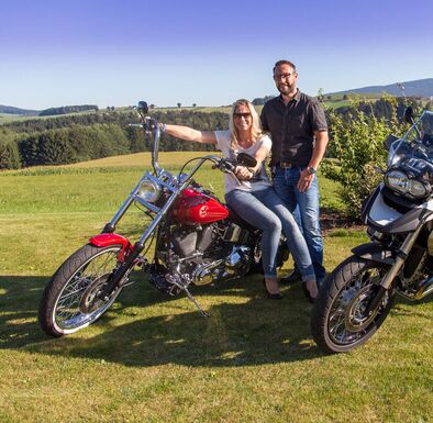 Paar sitzt auf Motorrad, welches im Wellnessgarten steht