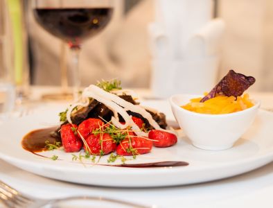 Ein Teller mit Schmorbraten, roten Gnocchi und Tagliatelle und ein Glas Rotwein