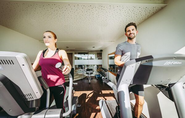 Pärchen trainiert auf Laufband und Crosstrainer im Fitnessraum